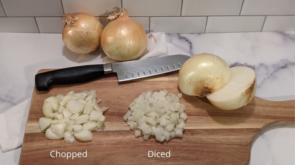 A cutting board with two small piles of onion displaying what chopped onion and diced onion looks like. 