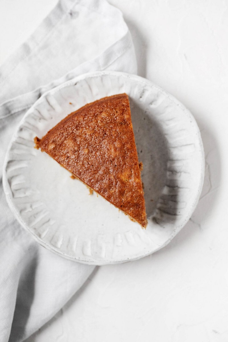 An overhead image of a triangular slice of gingerbread, laid out on a dessert plate with a gray napkin.