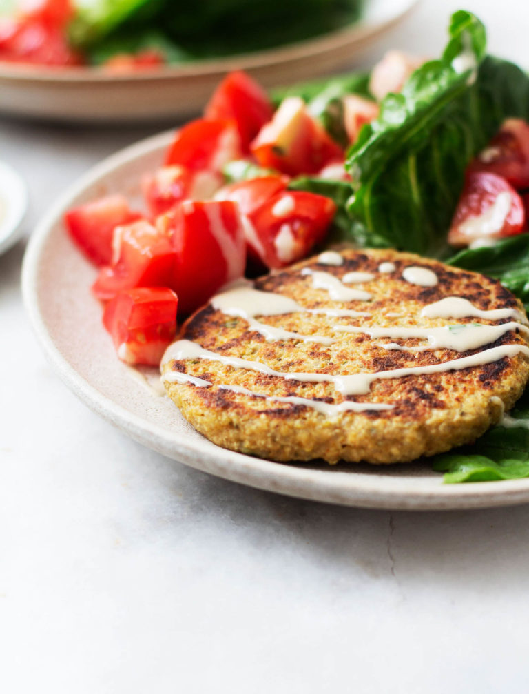 A side angled photograph of a quinoa chickpea zaatar burger patty, served with lettuce wraps and tahini dressing.