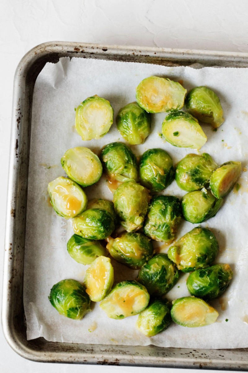 A parchment lined baking sheet is topped with raw vegetables in a buttery glaze.