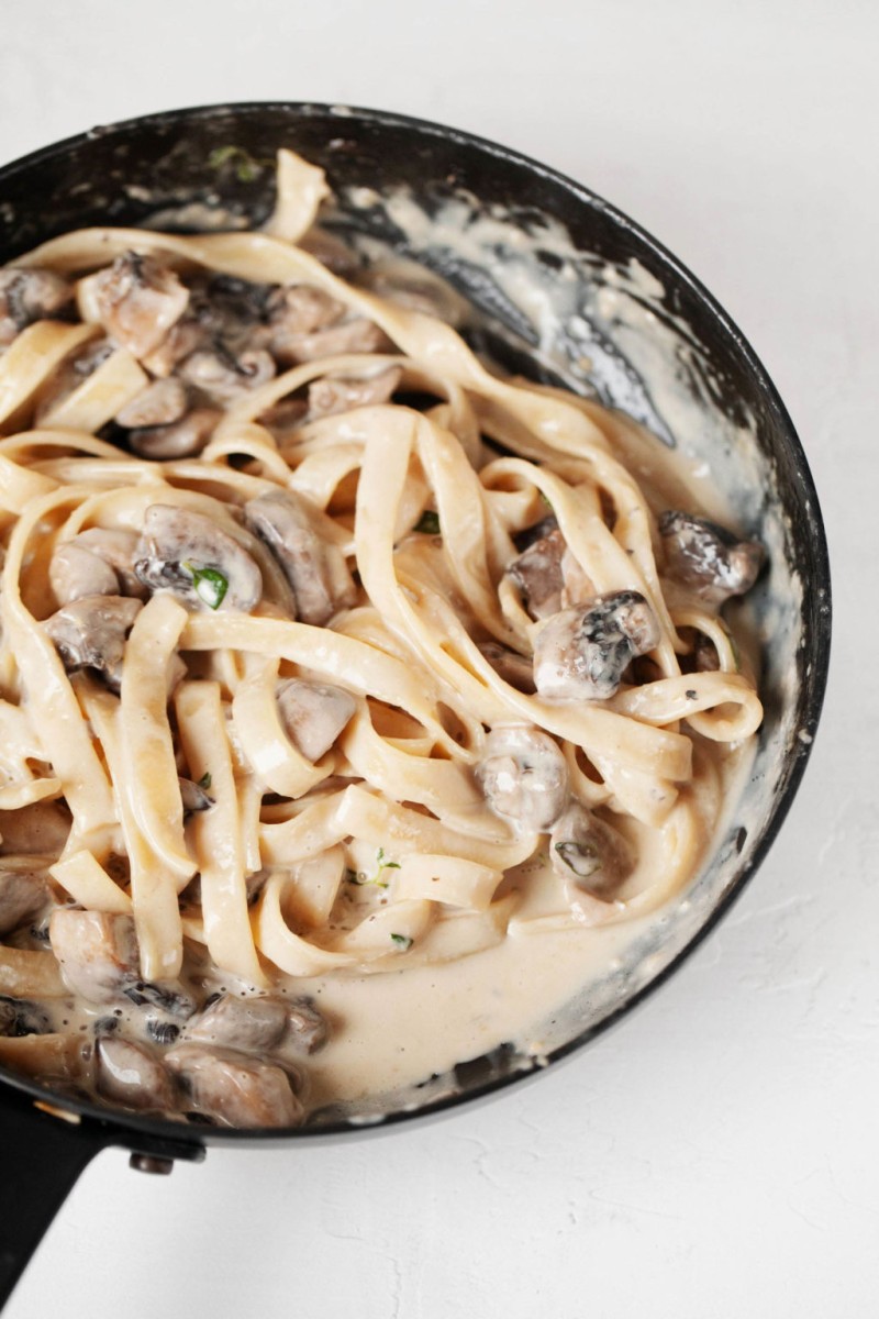 A black skillet is filled with fettucine, herbs, and a white pasta sauce.