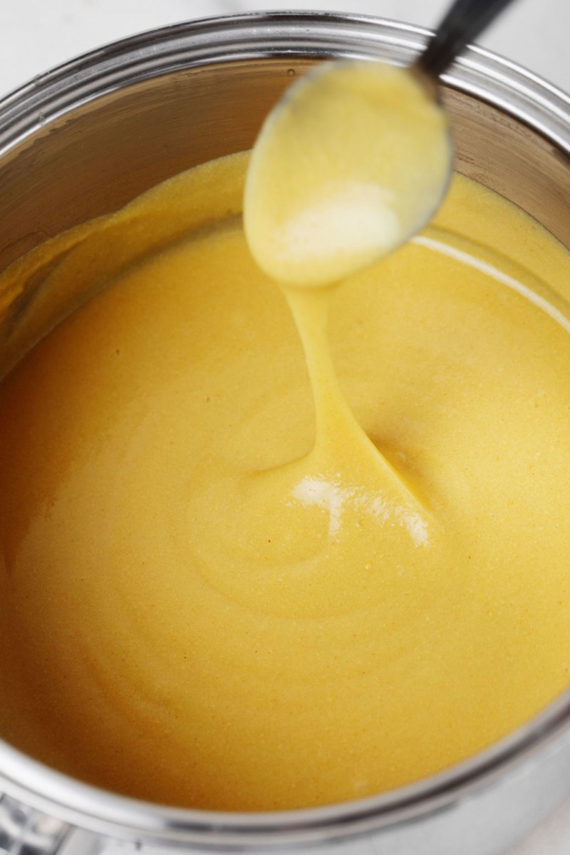 A vegan cheddar cheese sauce is being prepared in a metal saucepan.