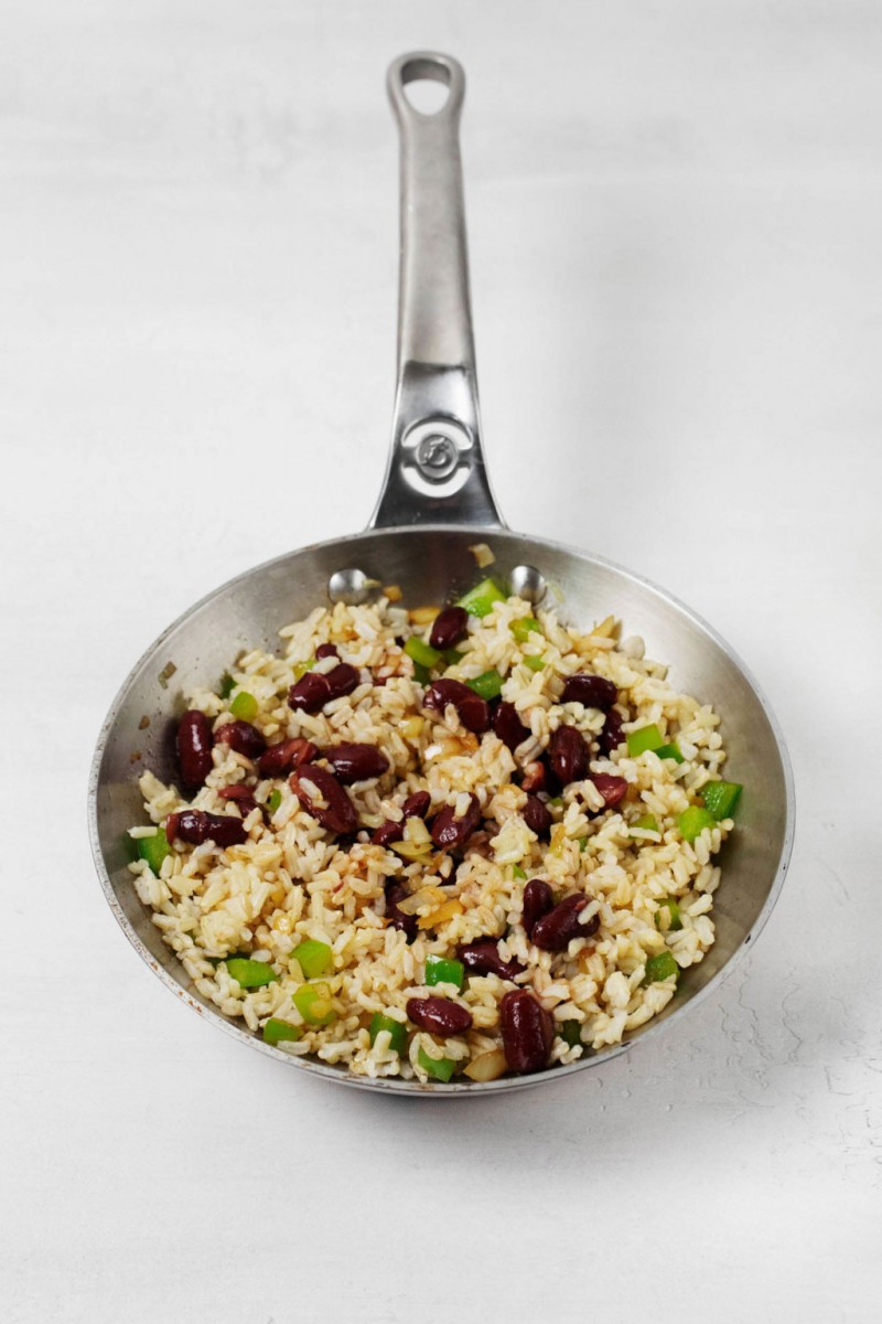 A small, steel saute pan holds a mixture of grains, vegetables, and beans.