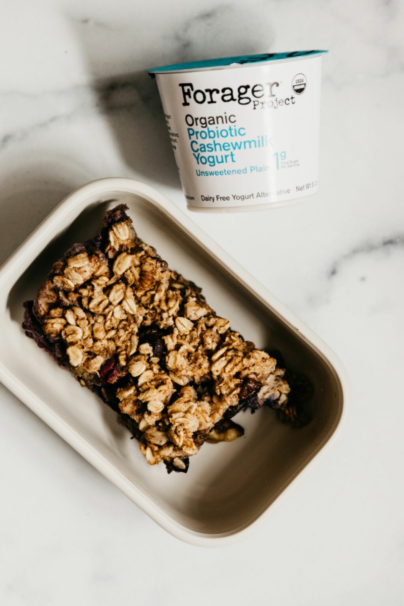 A portion of baked oatmeal has been served in a small container. There's a container of yogurt nearby.