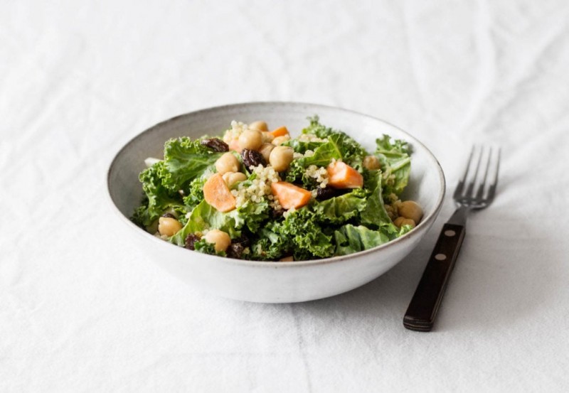 A salad with greens and chickpeas is held in a white serving bowl, with a fork resting nearby.