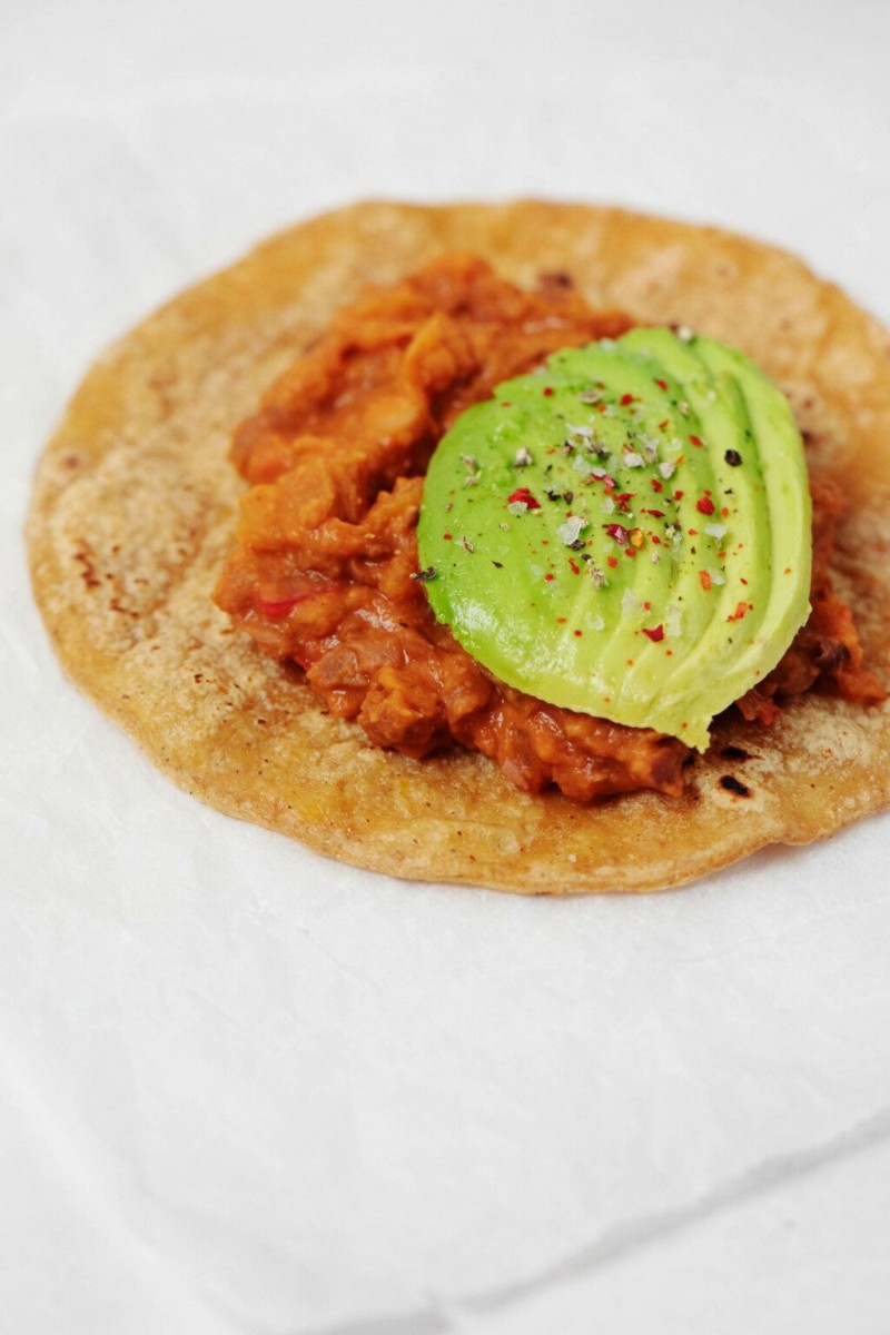 A corn tortilla has been topped with a smoky bean spread and half a sliced avocado. 