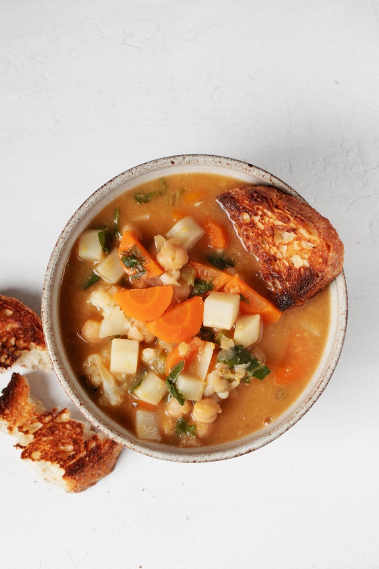 A white soup bowl is filled with a miso vegetable stew. Small pieces of toast are in the soup and lying next to the soup bowl.