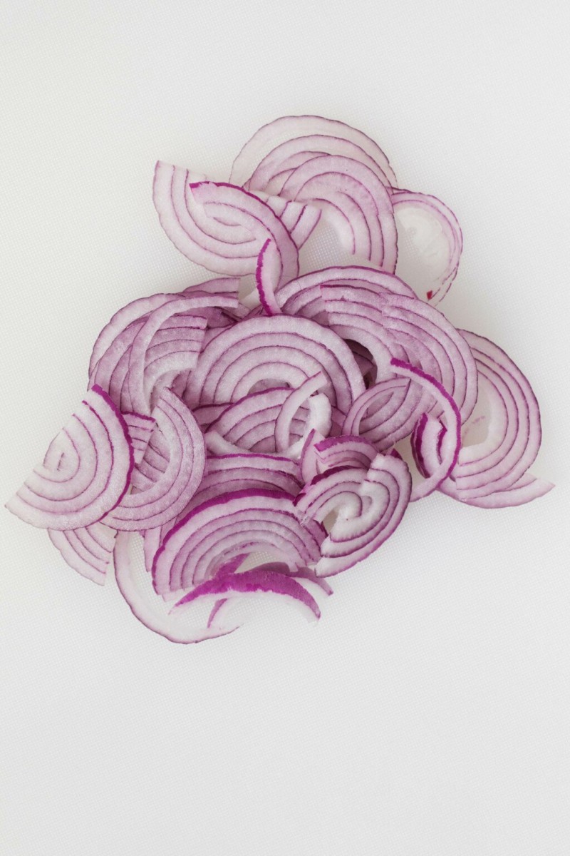 Thinly sliced red onions are laid out on a white surface.