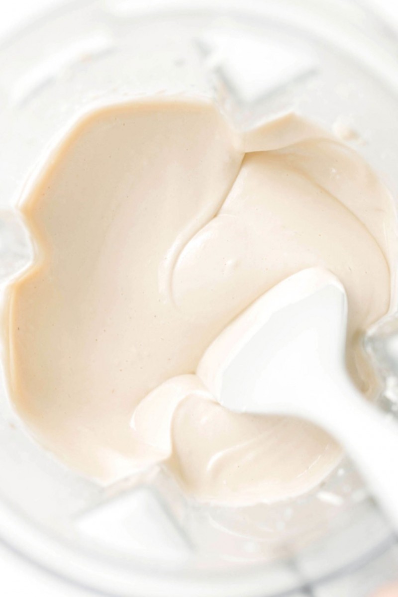 A creamy, blended tofu whipped cream is being stirred in the blender container with a spatula.