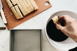 A rectangular slice of cake is being dipped in a coffee-based liquid mixture.