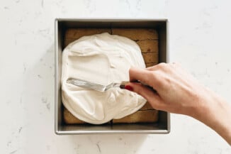 A thick white cream is being spread over cake.