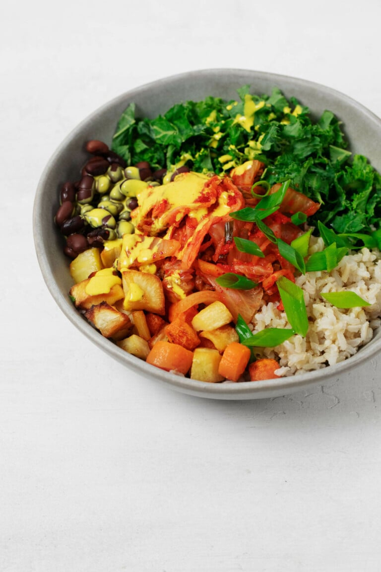 A vibrant bowl of vegetables, legumes, and cultured cabbage has been served in a gray plate. It rests on a white surface.