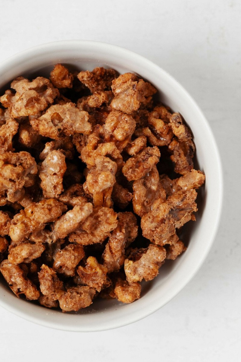 A close up, overhead image of vegan candied walnuts, which are served in a small, round white bowl.