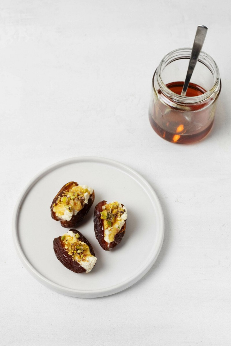 A jar of warm, herb-infused syrup is placed next to a small, white serving plate with stuffed dates.