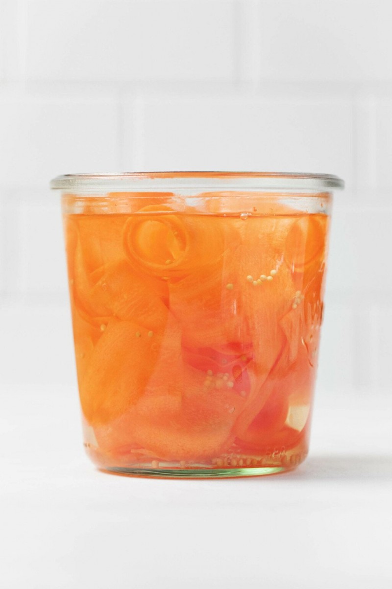 An angled photograph of a Weck mason jar, which is holding orange, pickled carrot ribbons.