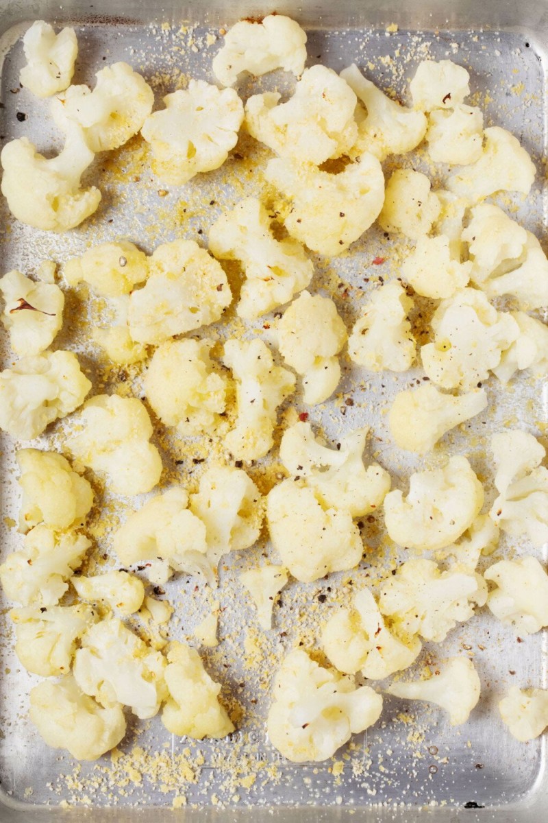 An overhead image of white cauliflower florets, which are midway through roasting. They've just been seasoned with salt and pepper.