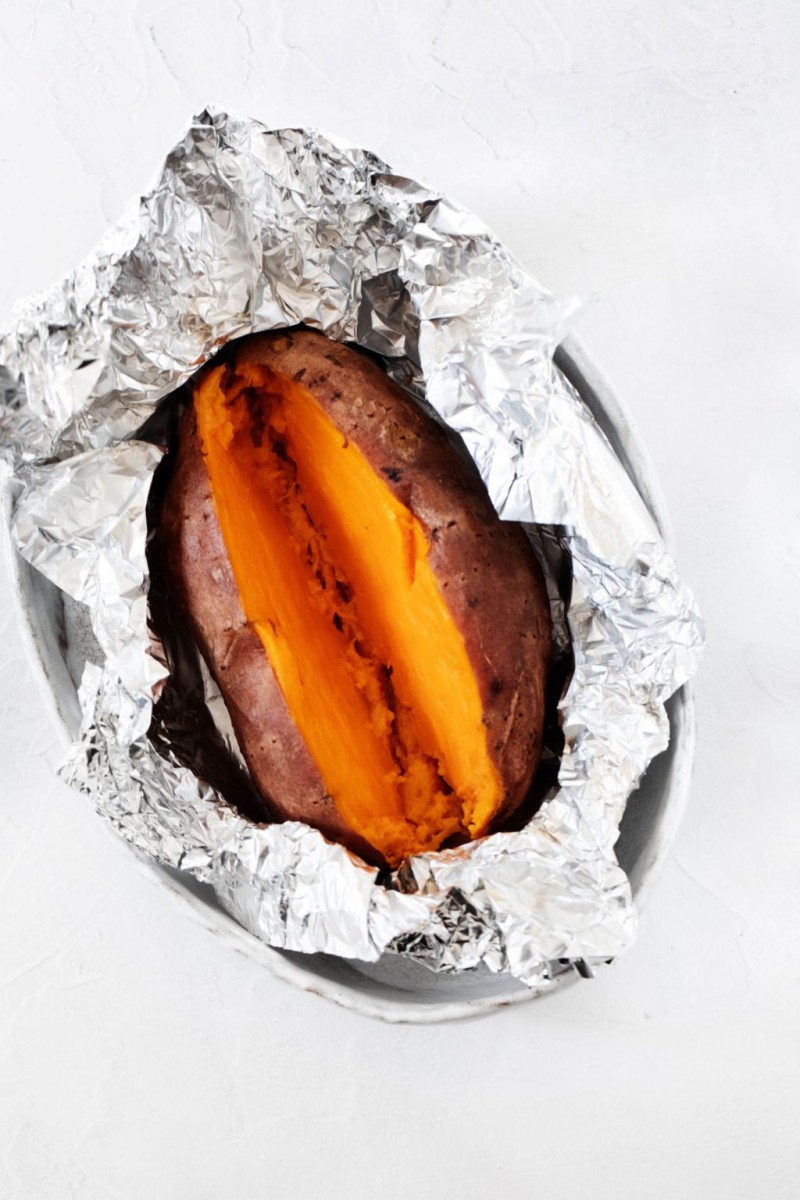 A roasted sweet potato is being stored in crumpled aluminum foil.