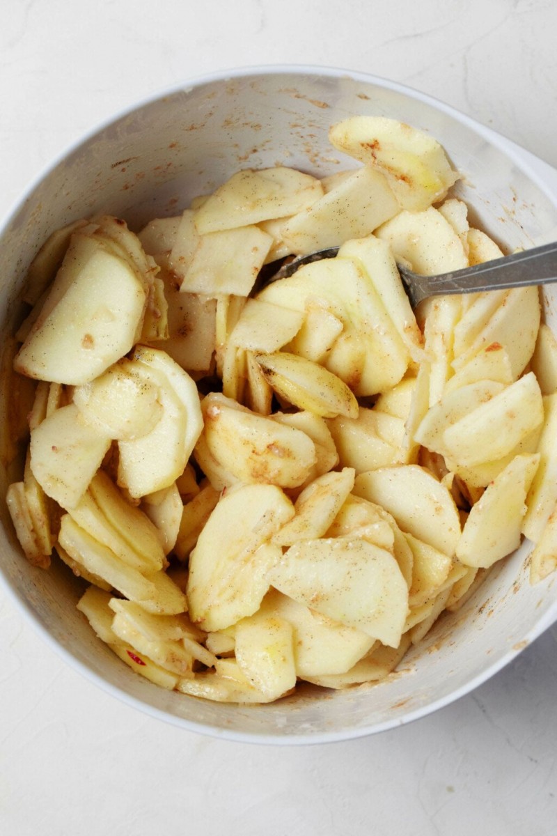 An overhead image of a large, white mixing bowl that's filled with thinly sliced apples.