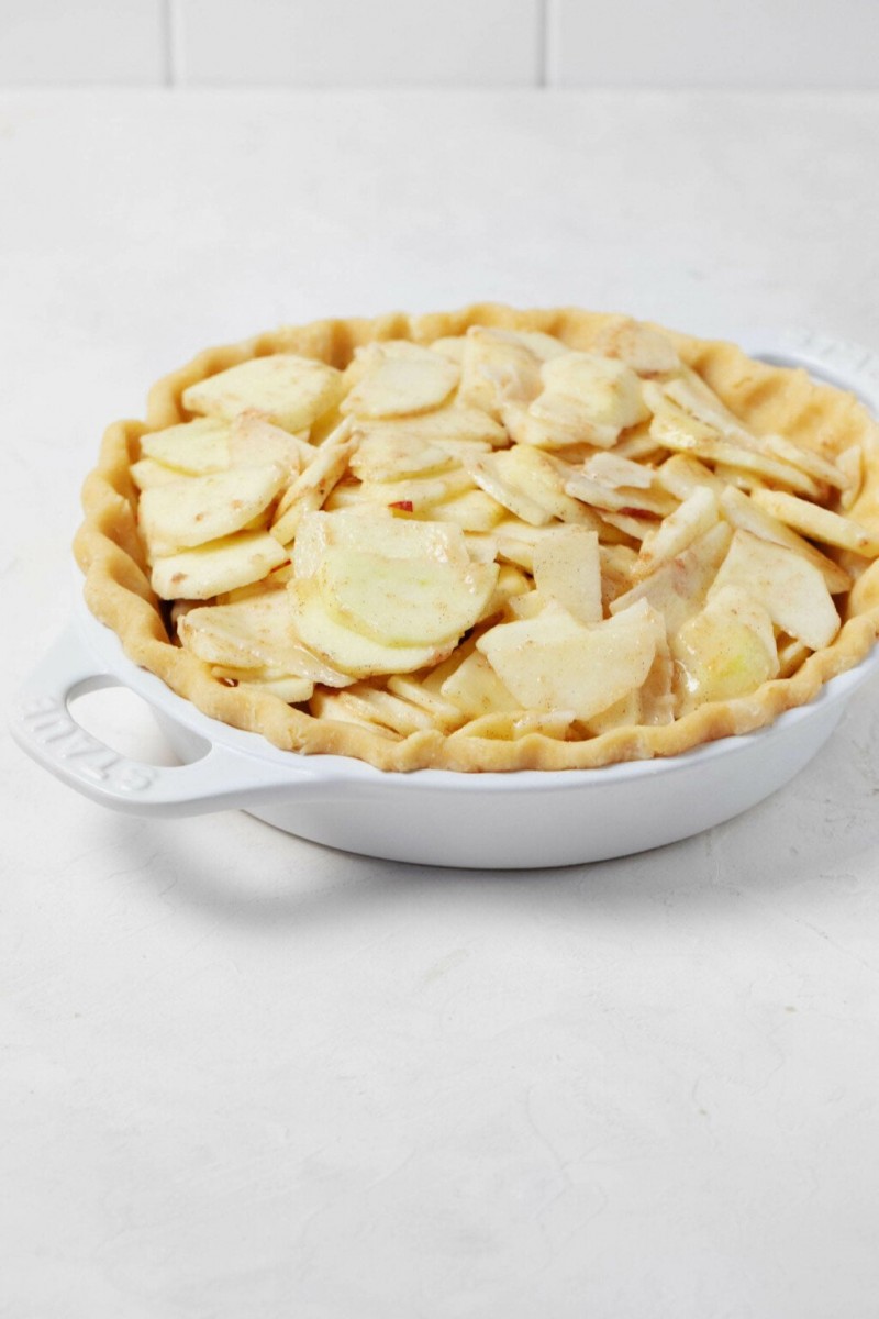 An angled image of a white pie plate, which has been filled with thinly sliced, glazed apples.