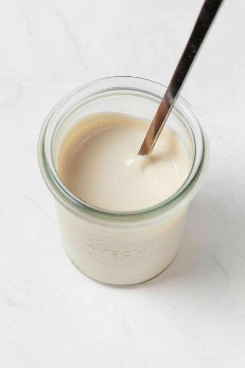 A Weck mason jar, resting on a white surface, holds a cream-colored tahini dressing.