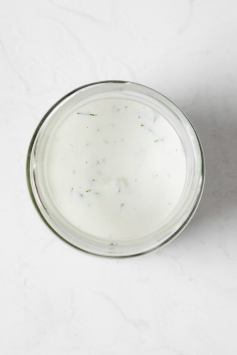 An overhead image of a glass jar, which has been filled with a white, creamy dressing. 