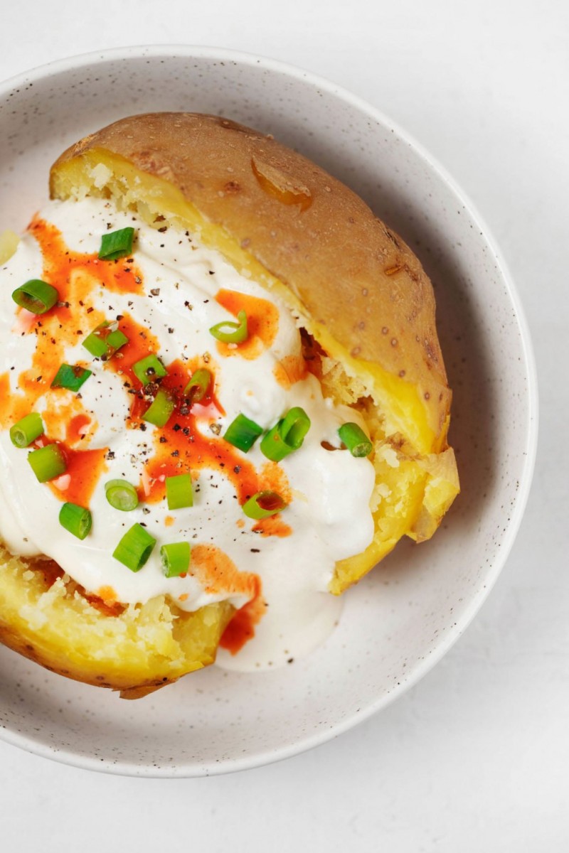 An overhead image of a split, baked potato, which is topped with chives, hot sauce, and other toppings.