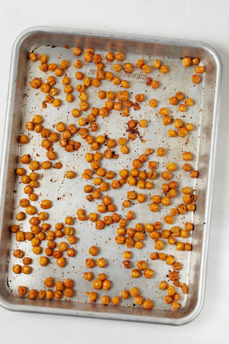 An aluminum baking sheet is covered in crispy roasted chickpeas, which have just been pulled from the oven.