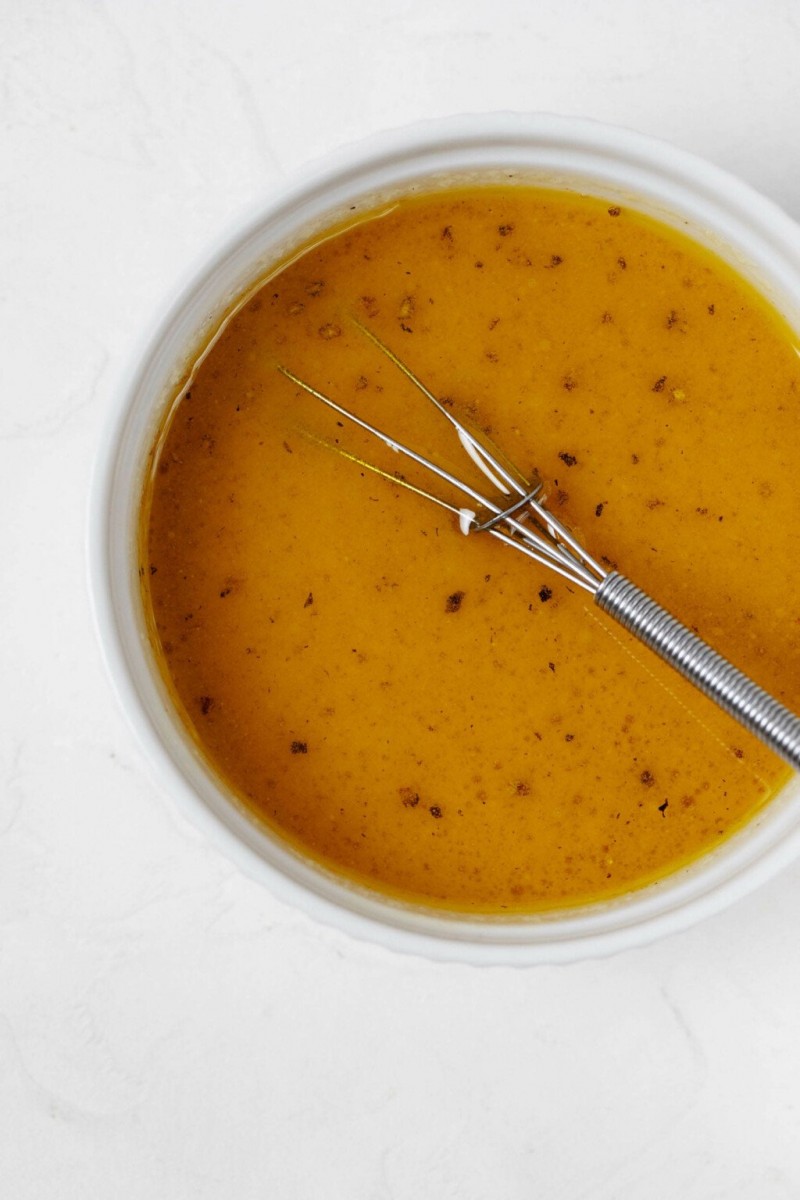 A small white bowl is being used to mix an orange and miso salad dressing. 