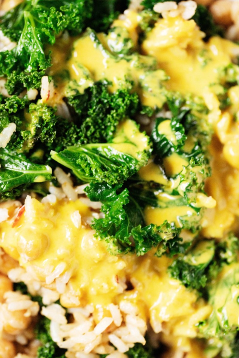 A closeup photograph of rice, chickpeas, kale, and a creamy yellow sauce.